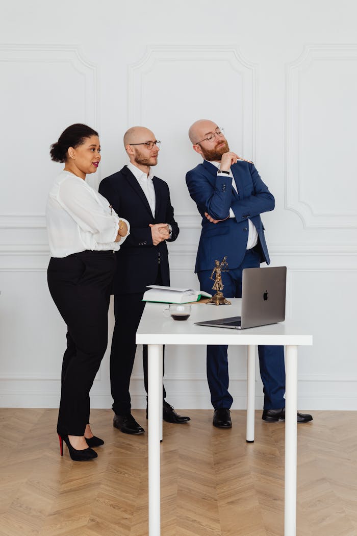 Three business professionals standing around a desk in a modern office setting, discussing strategies.
